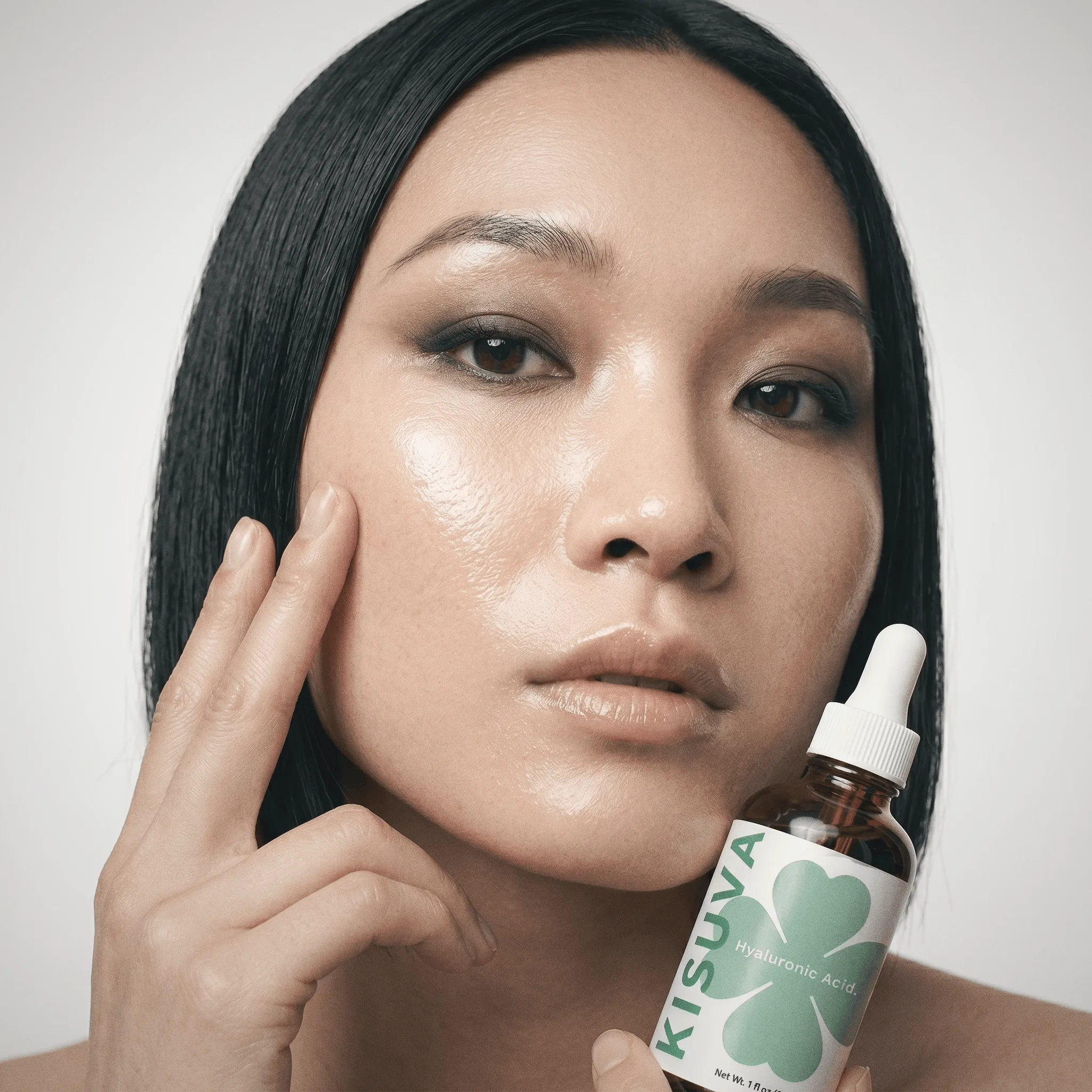 Woman with dewy hydrated skin holding Kisuva serum